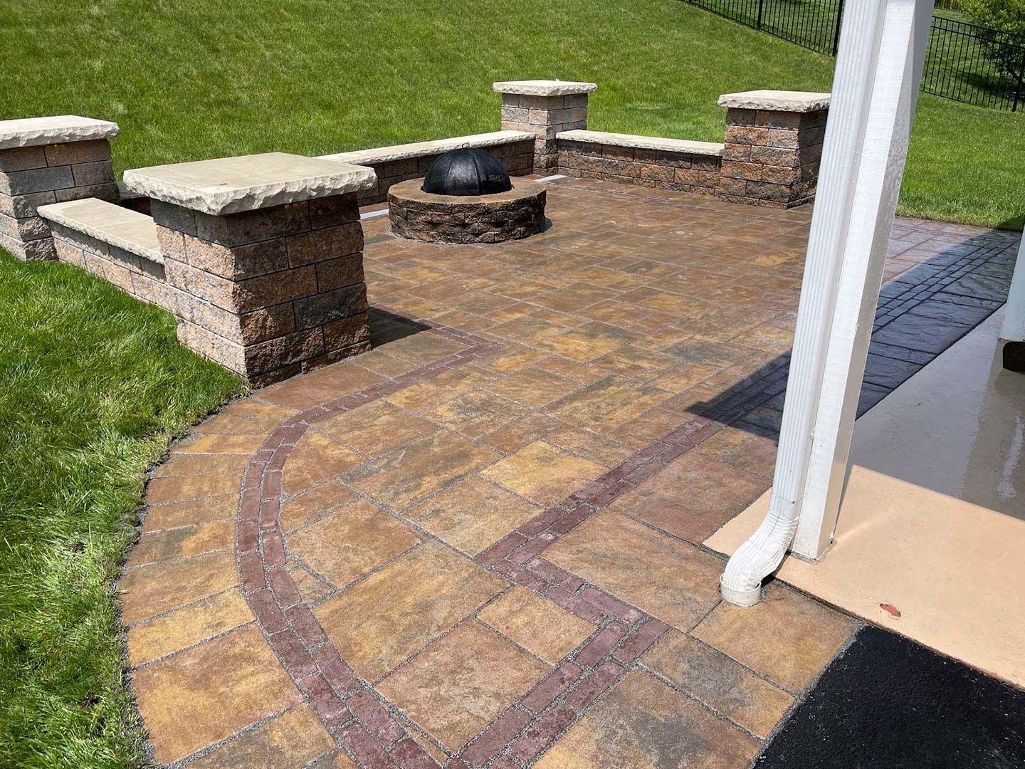 Brick patio with curved paver border, built-in stone benches, and a fire pit beside a house.