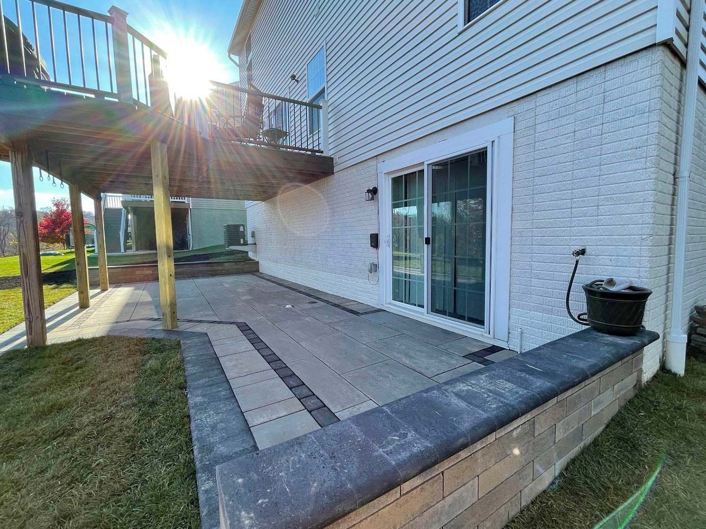 Back patio with sliding glass door, raised deck, and concrete walkway beside a house