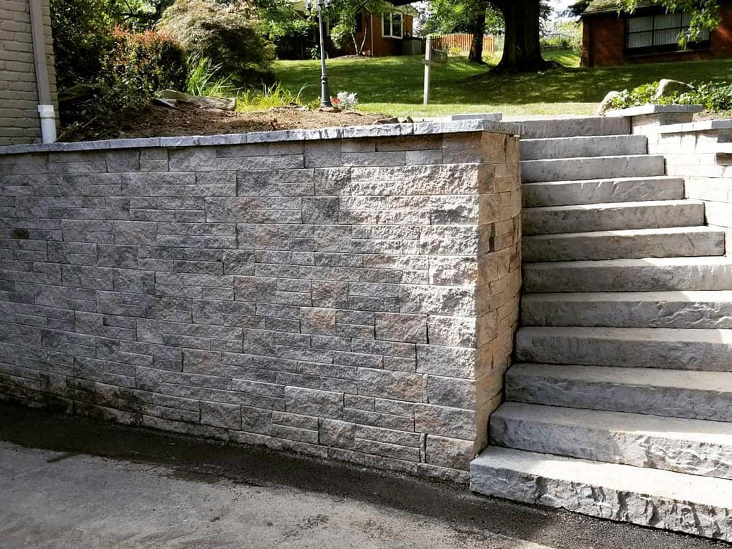 Stone retaining wall with concrete stairs leading up to a grassy yard and houses.