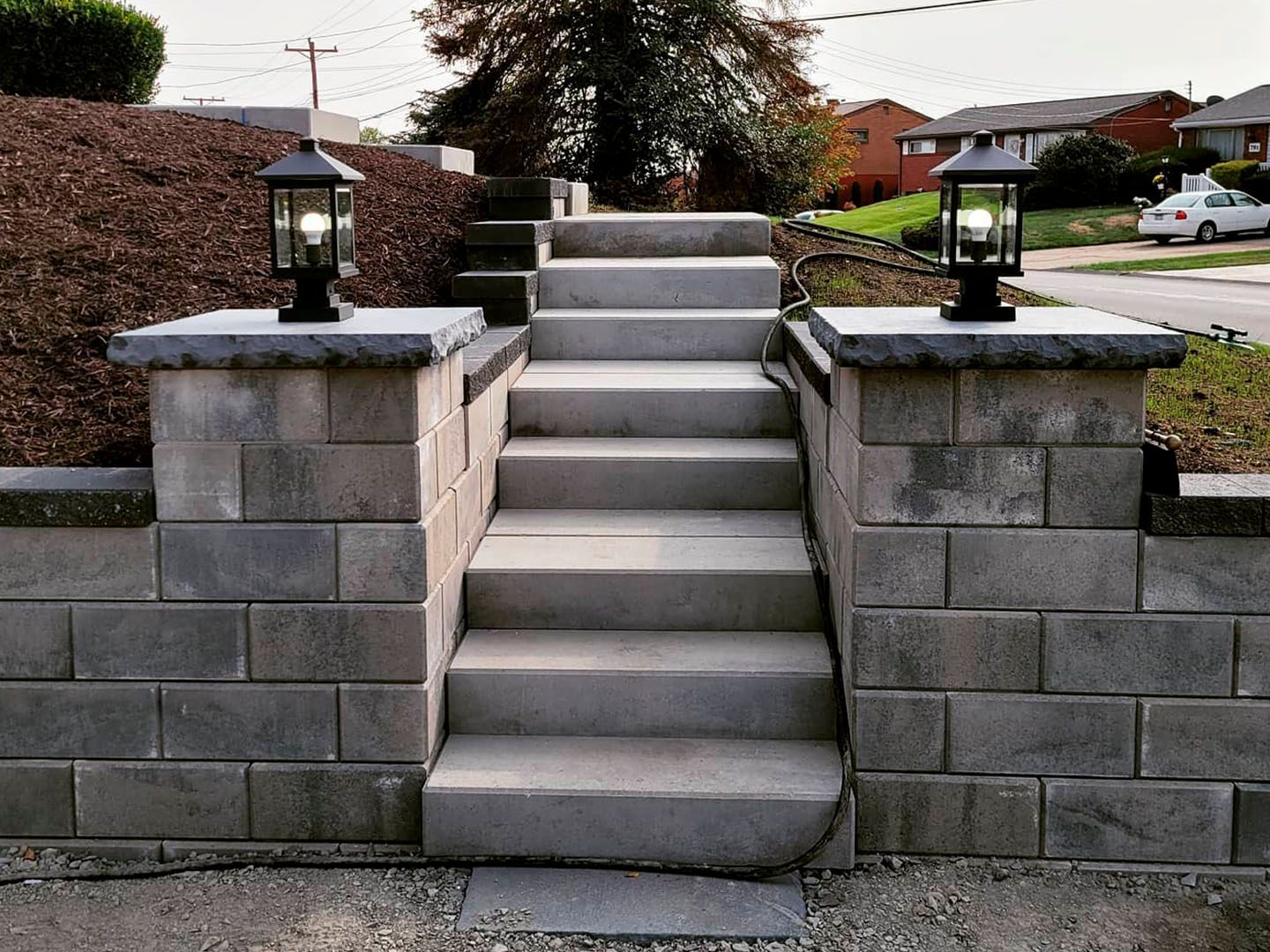 Stone front steps with lanterns between retaining walls leading up a residential yard
