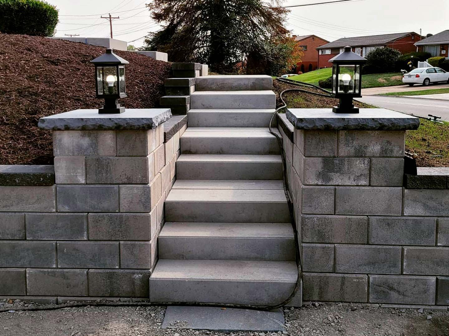 Stone front steps with brick retaining walls and two lanterns in a residential yard