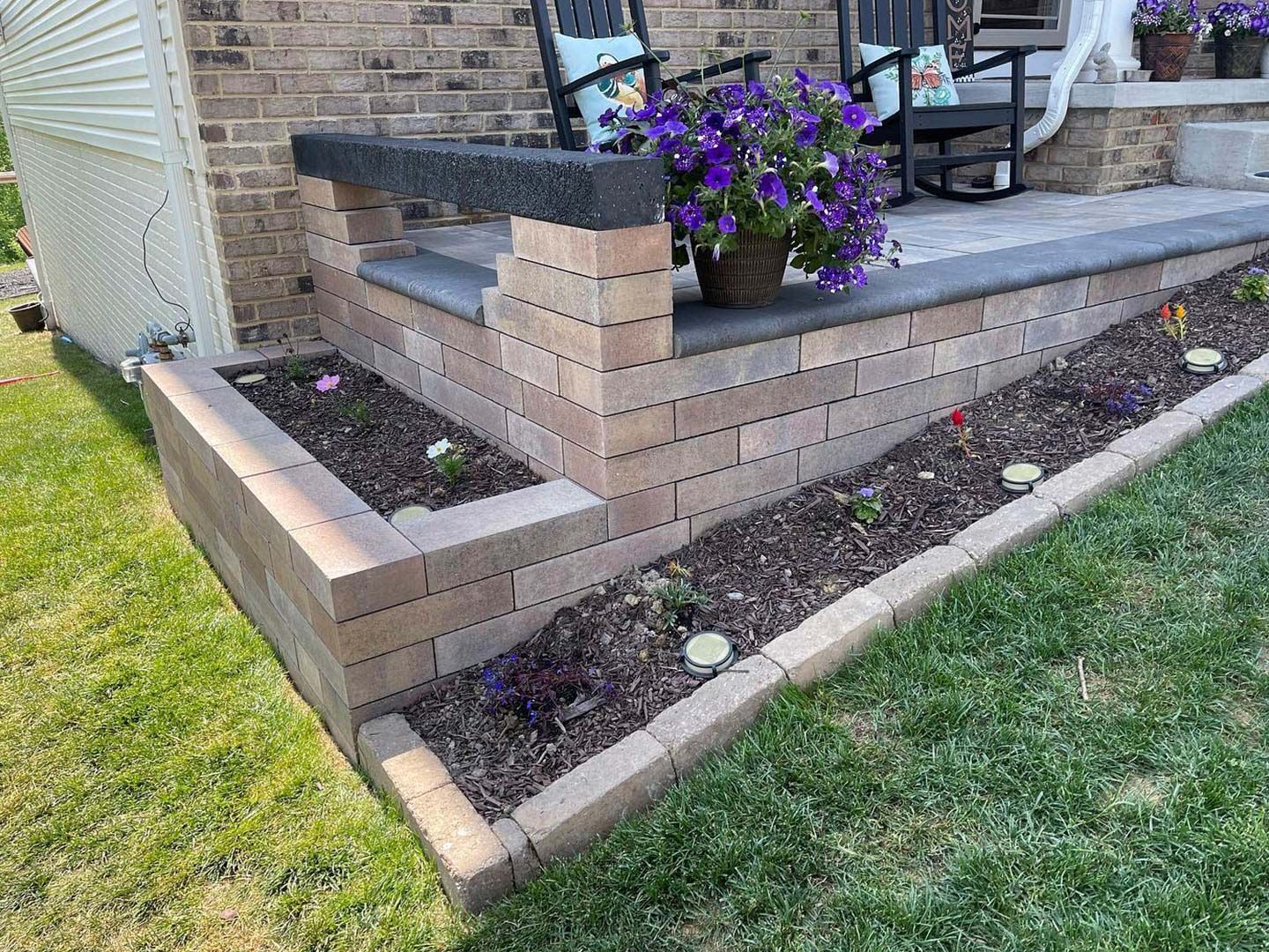 Brick porch with flower planter and curved retaining wall beside a grassy yard