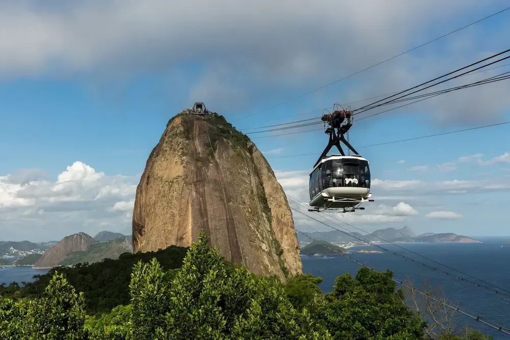Cable car gliding past Sugarloaf Mountain over Rio de Janeiro’s blue coastline under a clear sky