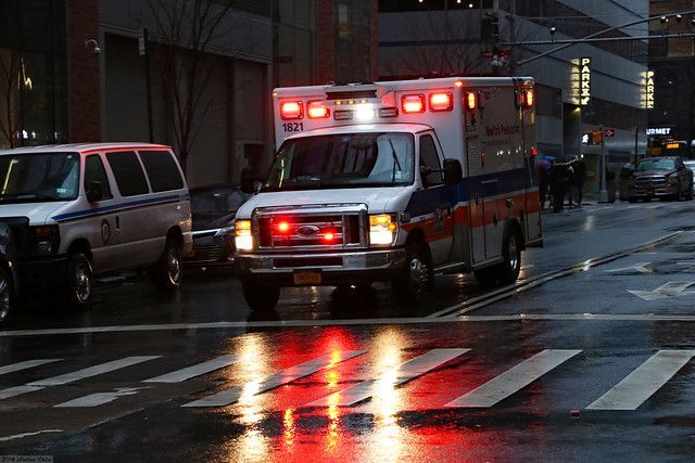 Ambulance with flashing lights driving on a wet city street at dusk