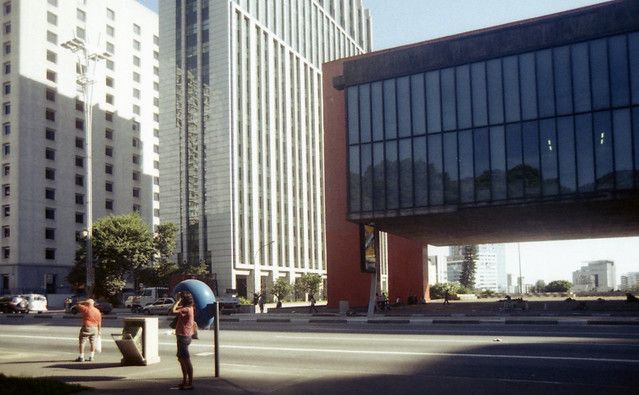 Cyclists in a city plaza beside tall modern office buildings on a sunny day
