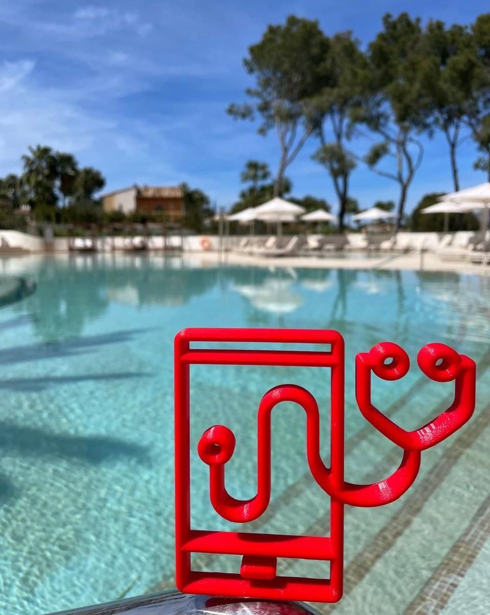Red phone and heart sculpture by a bright blue swimming pool with white umbrellas and trees.
