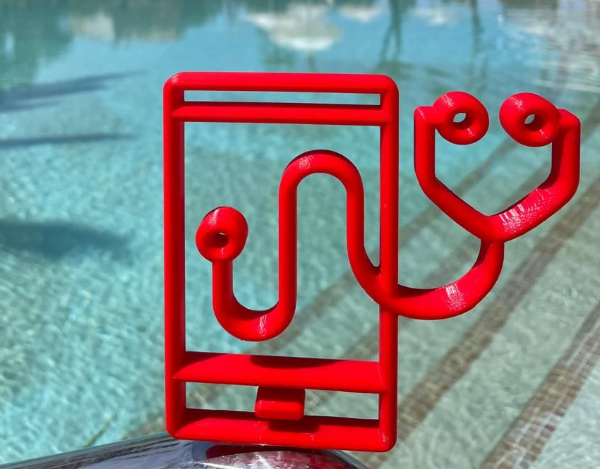 Red metal phone-shaped sculpture by a turquoise swimming pool in sunlight