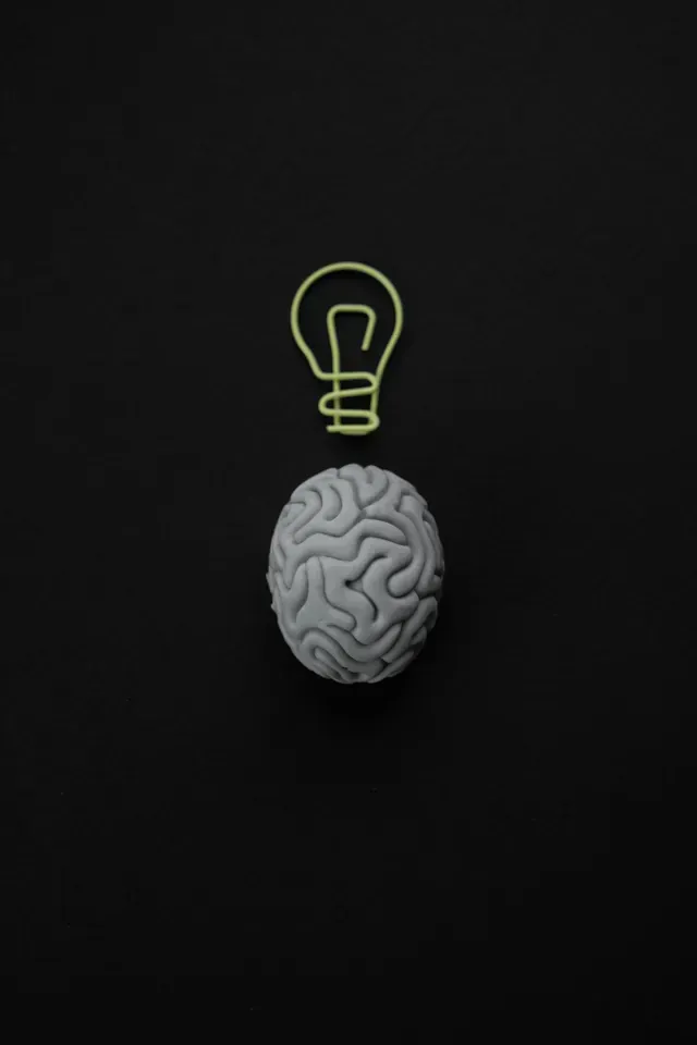 Gray brain beneath a glowing green lightbulb on a dark background