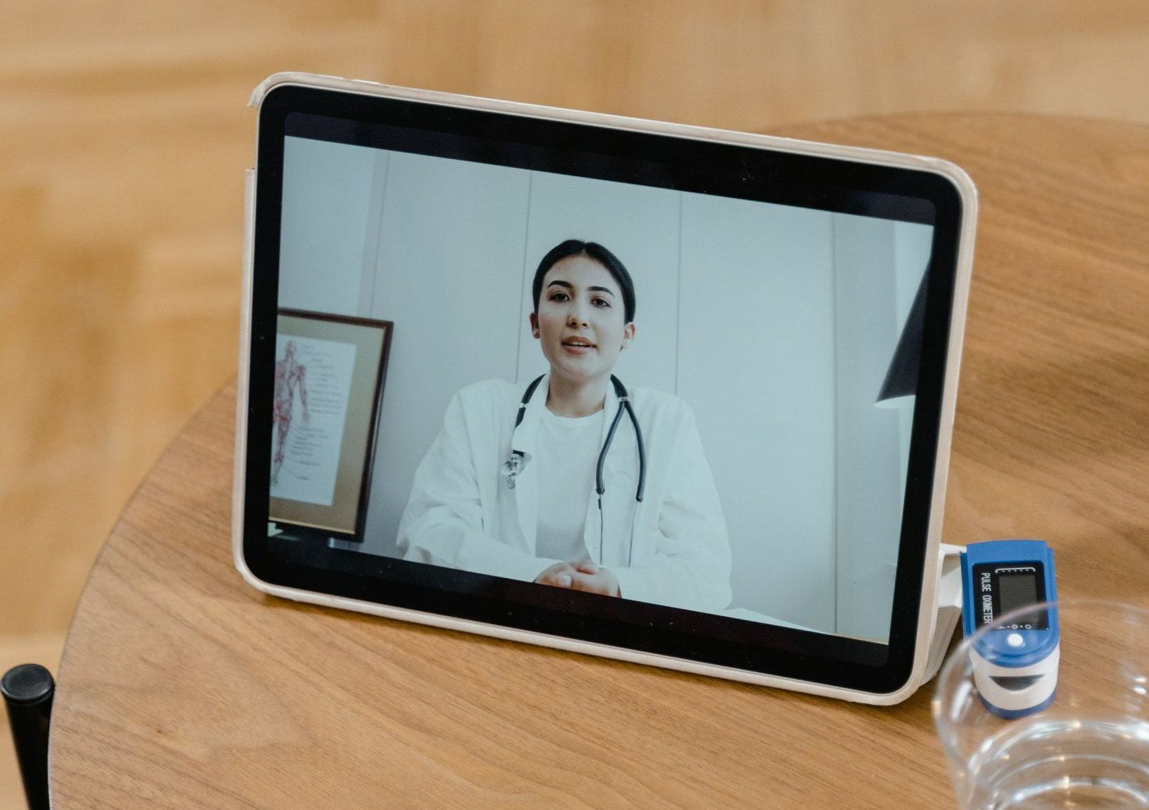 Tablet on a desk showing a doctor in a video call, with a small cup beside it