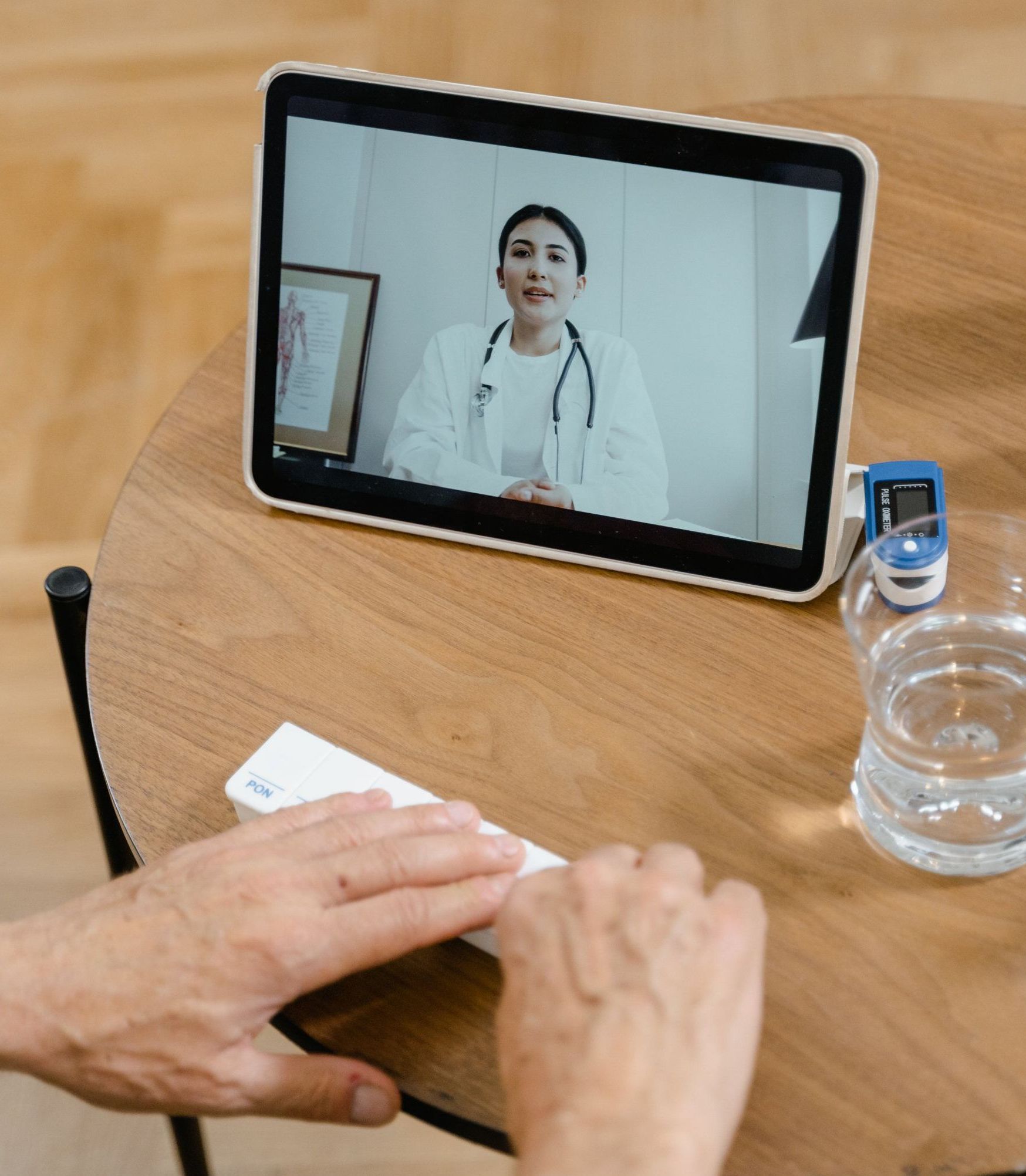 Video call with a doctor on a tablet beside a person writing at a wooden table.