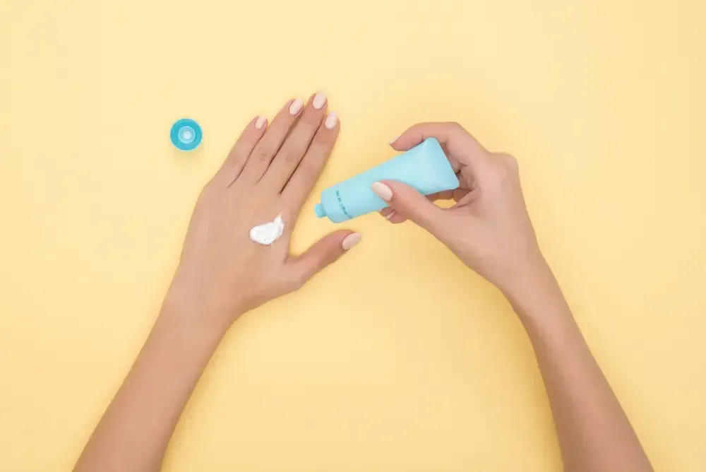 Hands applying sunscreen lotion on the back of a hand against a yellow background