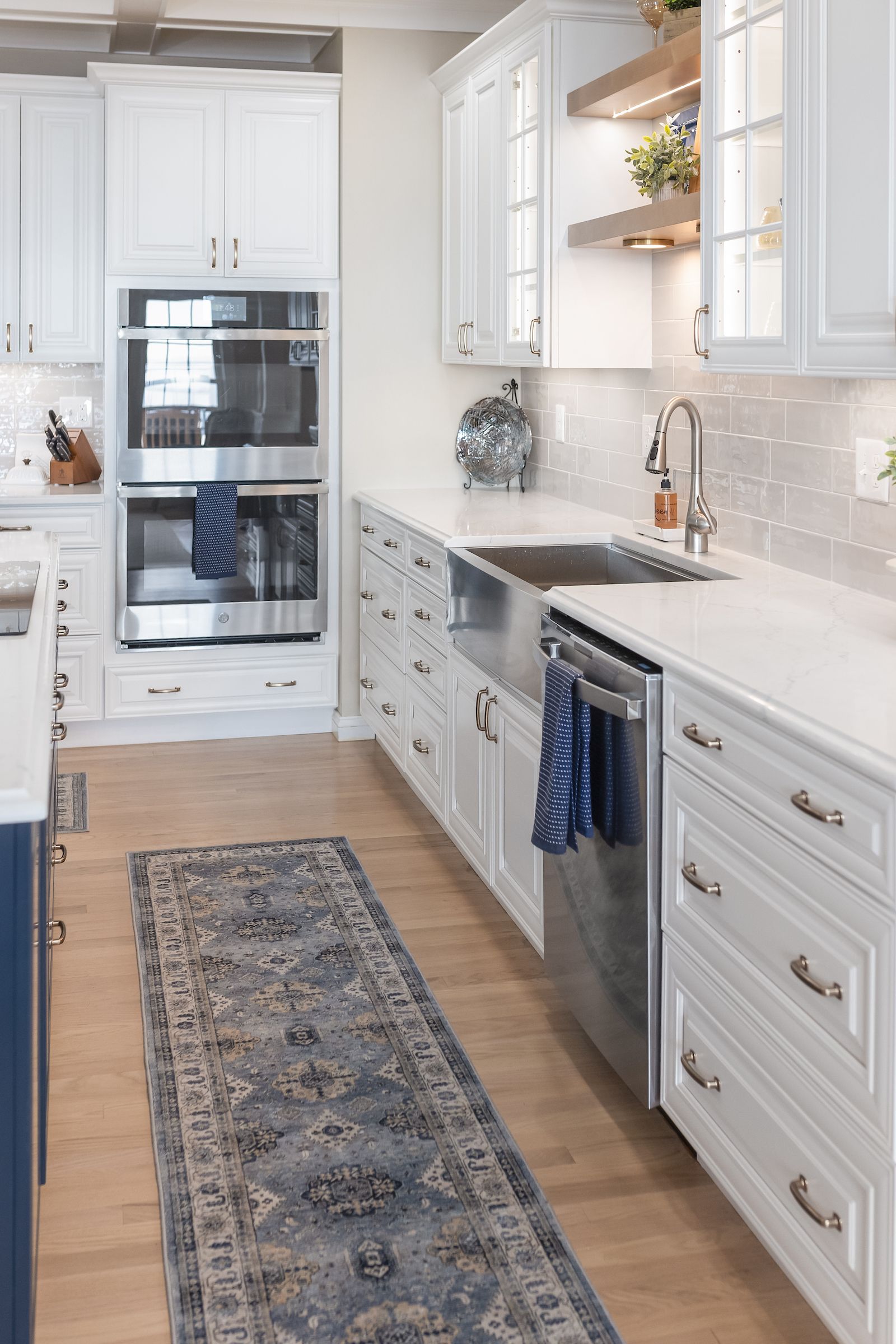 Calacatta Miraggio Cielo Q Quartz Countertops, Armonie Picadilly Avorio Glossy Tile Backsplash, Waypoint Painted Linen Perimeter Cabinets, Painted Navy Island Cabinets, and Maple Rye Floating Shelves