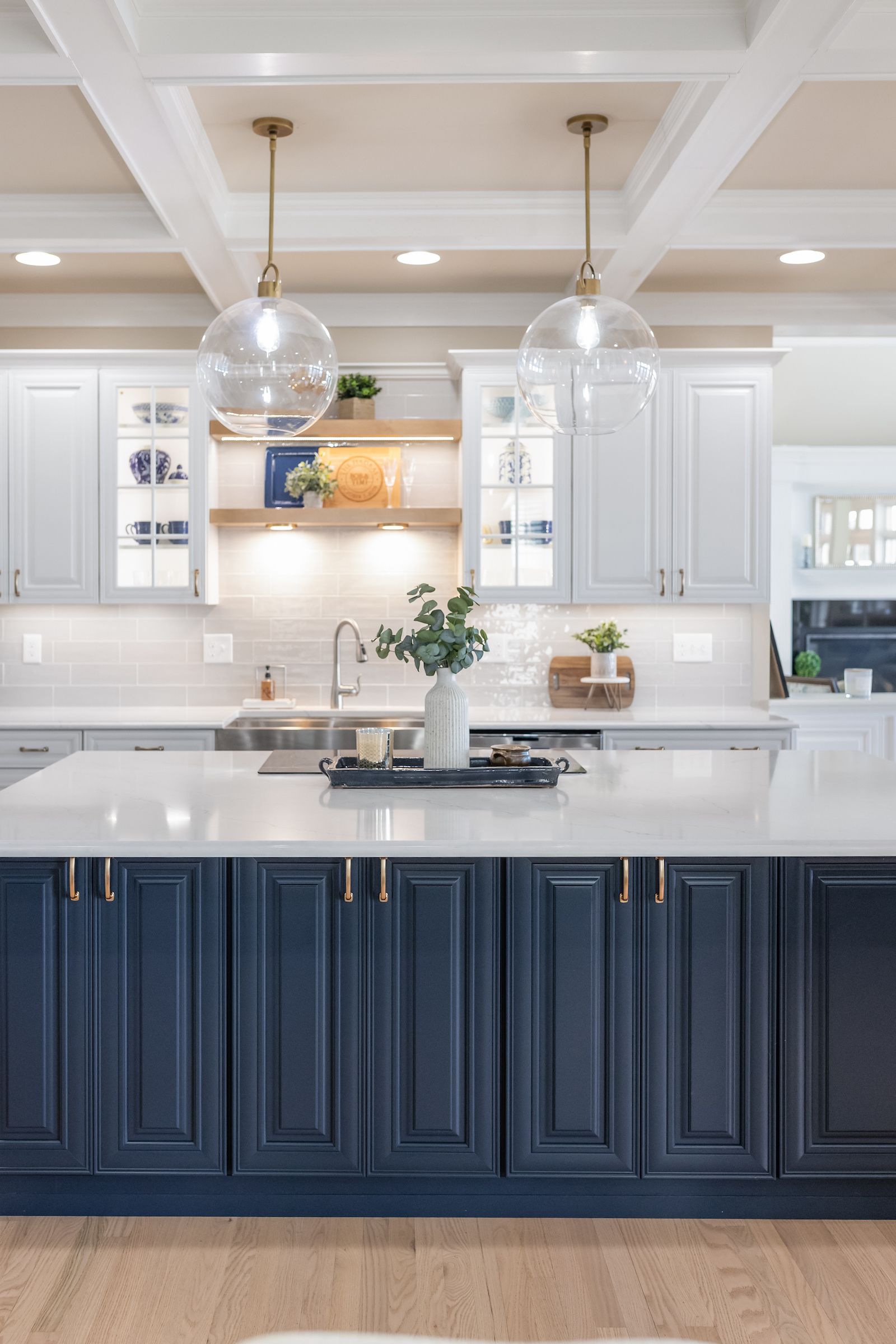 Calacatta Miraggio Cielo Q Quartz Countertops, Armonie Picadilly Avorio Glossy Tile Backsplash, Waypoint Painted Linen Perimeter Cabinets, Painted Navy Island Cabinets, and Maple Rye Floating Shelves