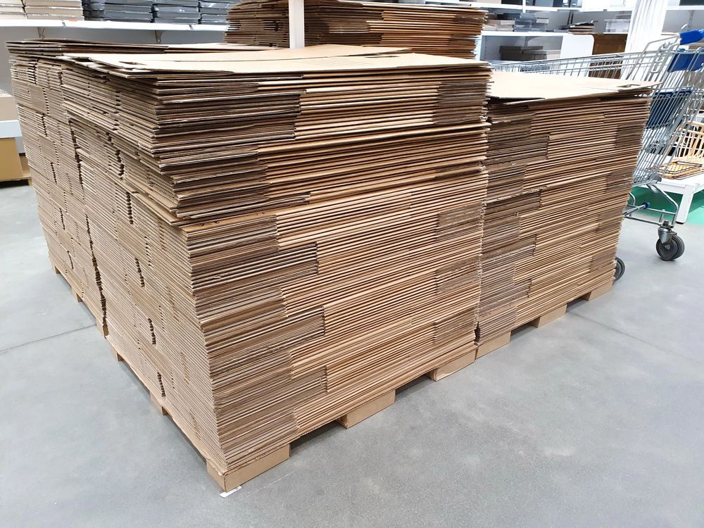 Láminas de cartón marrón apiladas sobre un palé de madera, en un entorno industrial.
