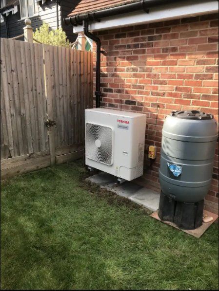 An air source heat pump and water butt next to a brick wall and wooden fence on a lawn.