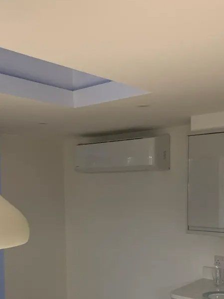 White air conditioning unit on a white wall in a room with a recessed ceiling and lights.
