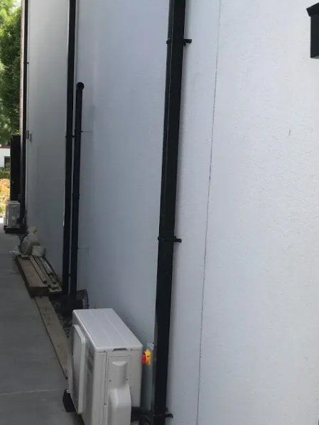 White building exterior with black pipes and an air conditioning unit.