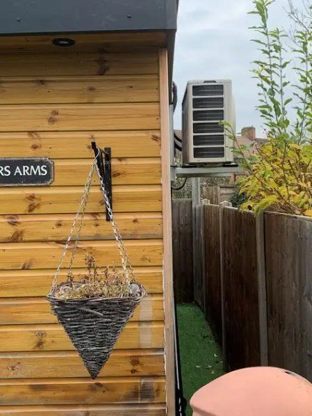 Wooden shed with hanging basket, air conditioning unit, and fence.
