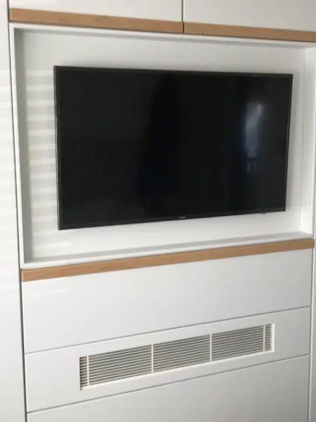 White cabinet with recessed TV, ventilation grate, and wood trim.