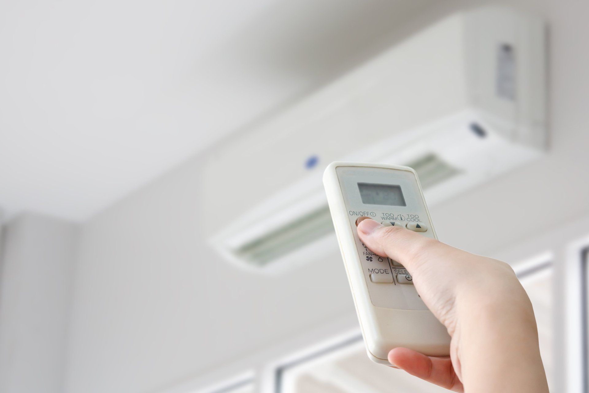 Hand with remote control aimed at a wall-mounted air conditioner.