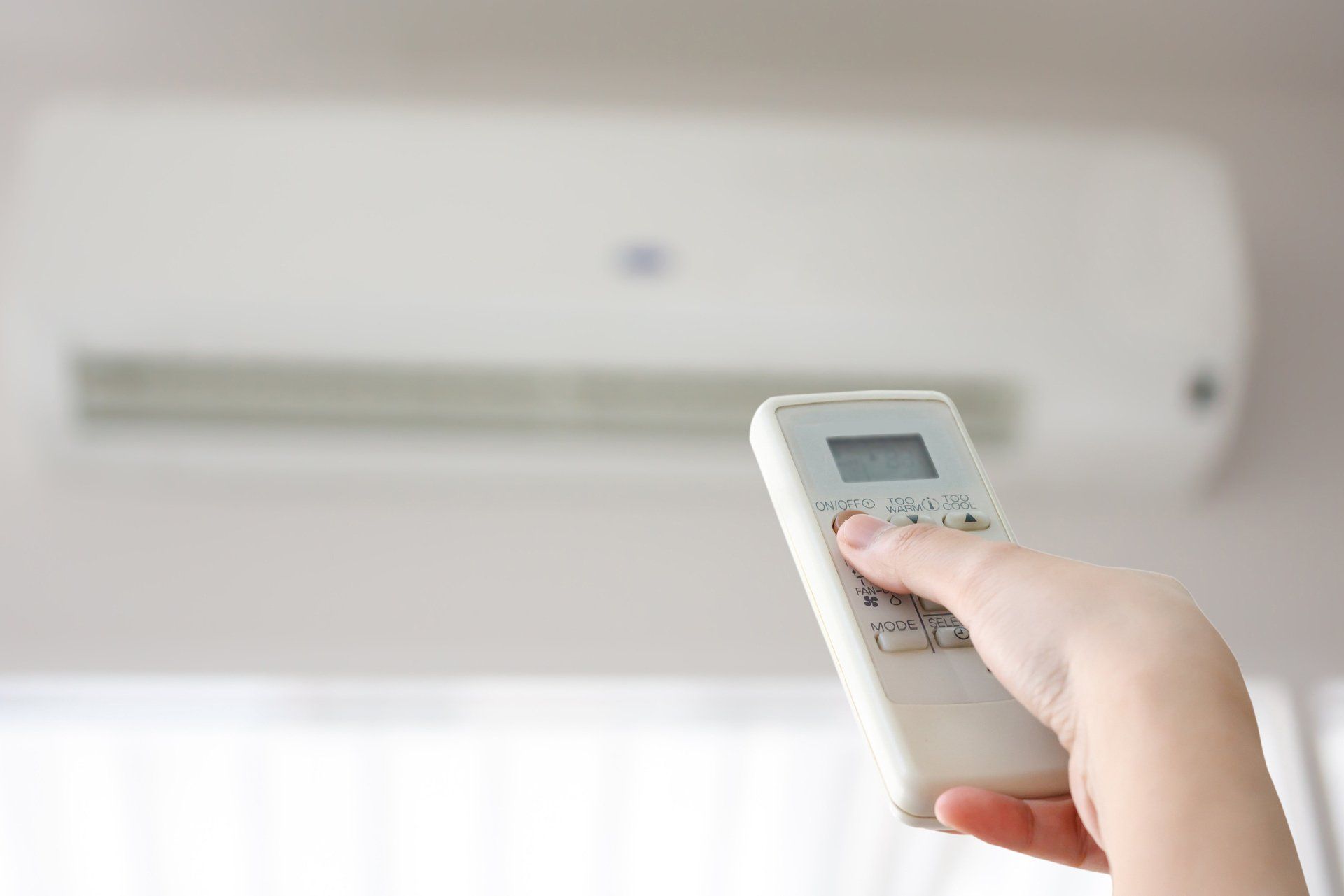 Hand holding a remote control, aiming at a white air conditioner on a wall.