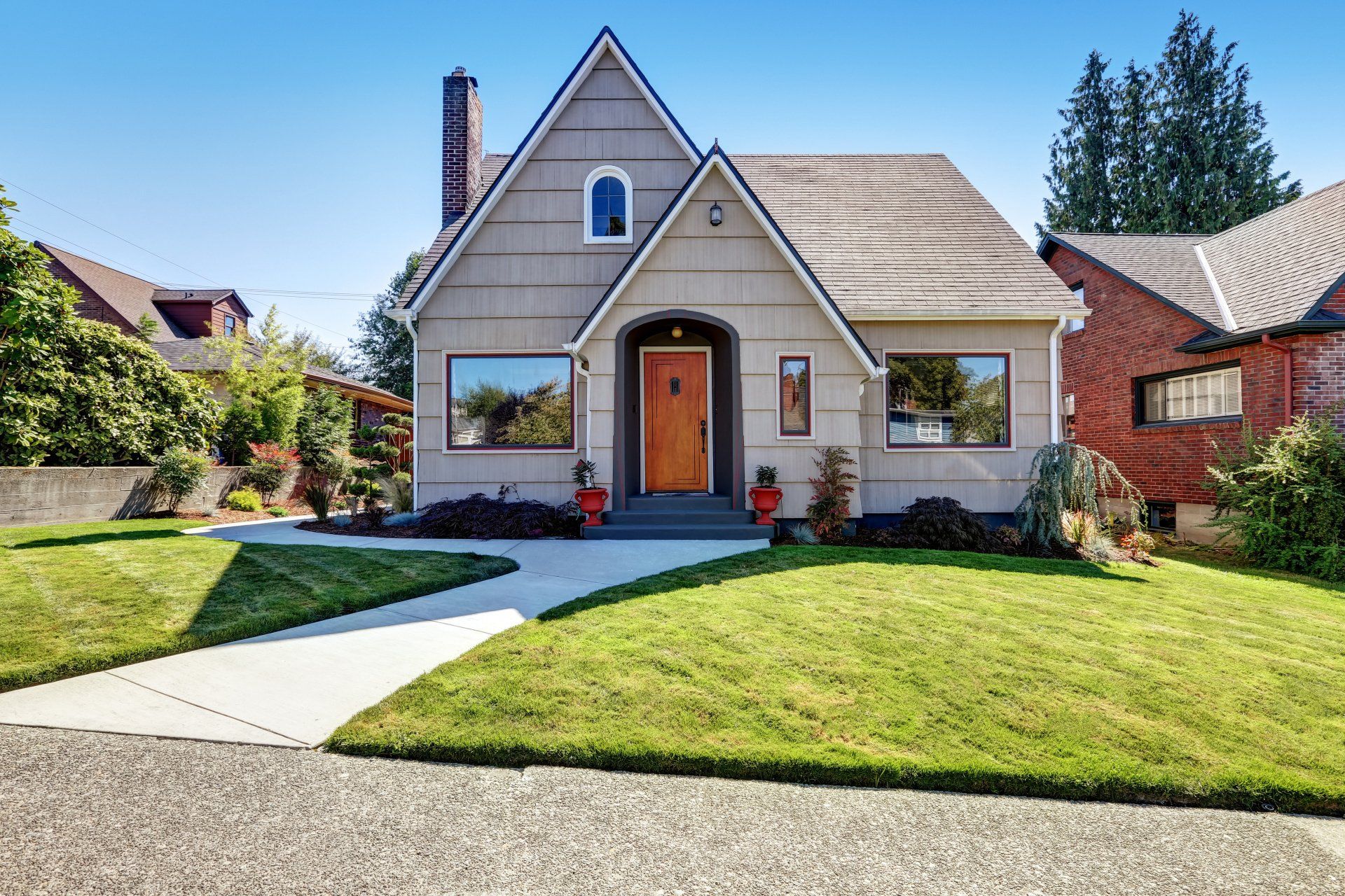 A tan, two-story house with a gabled roof and orange door, surrounded by green grass and a paved walkway.