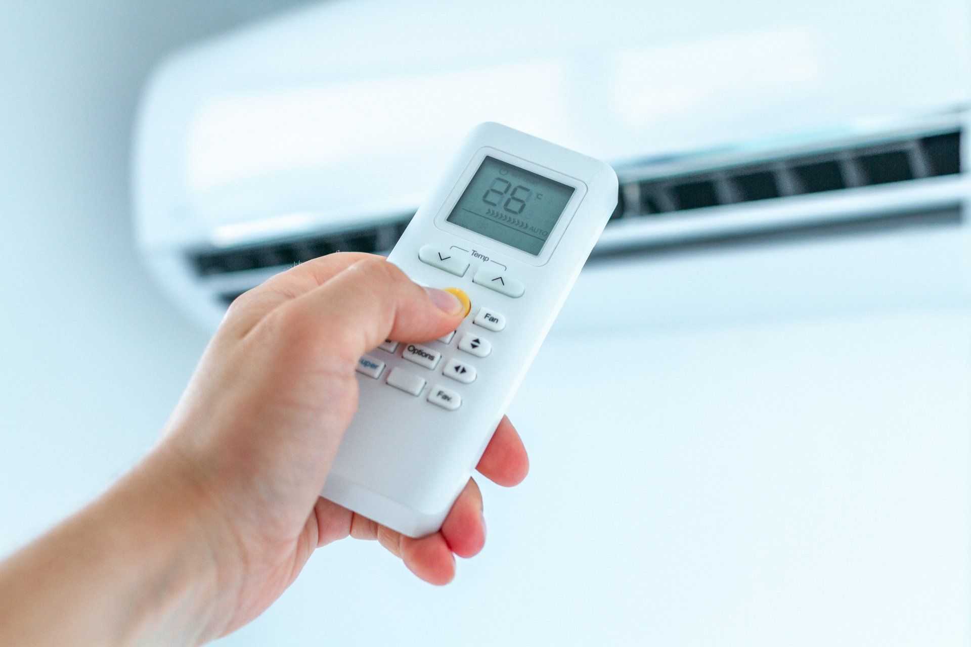 Hand holding a white remote, adjusting the temperature of a white air conditioner on a wall.