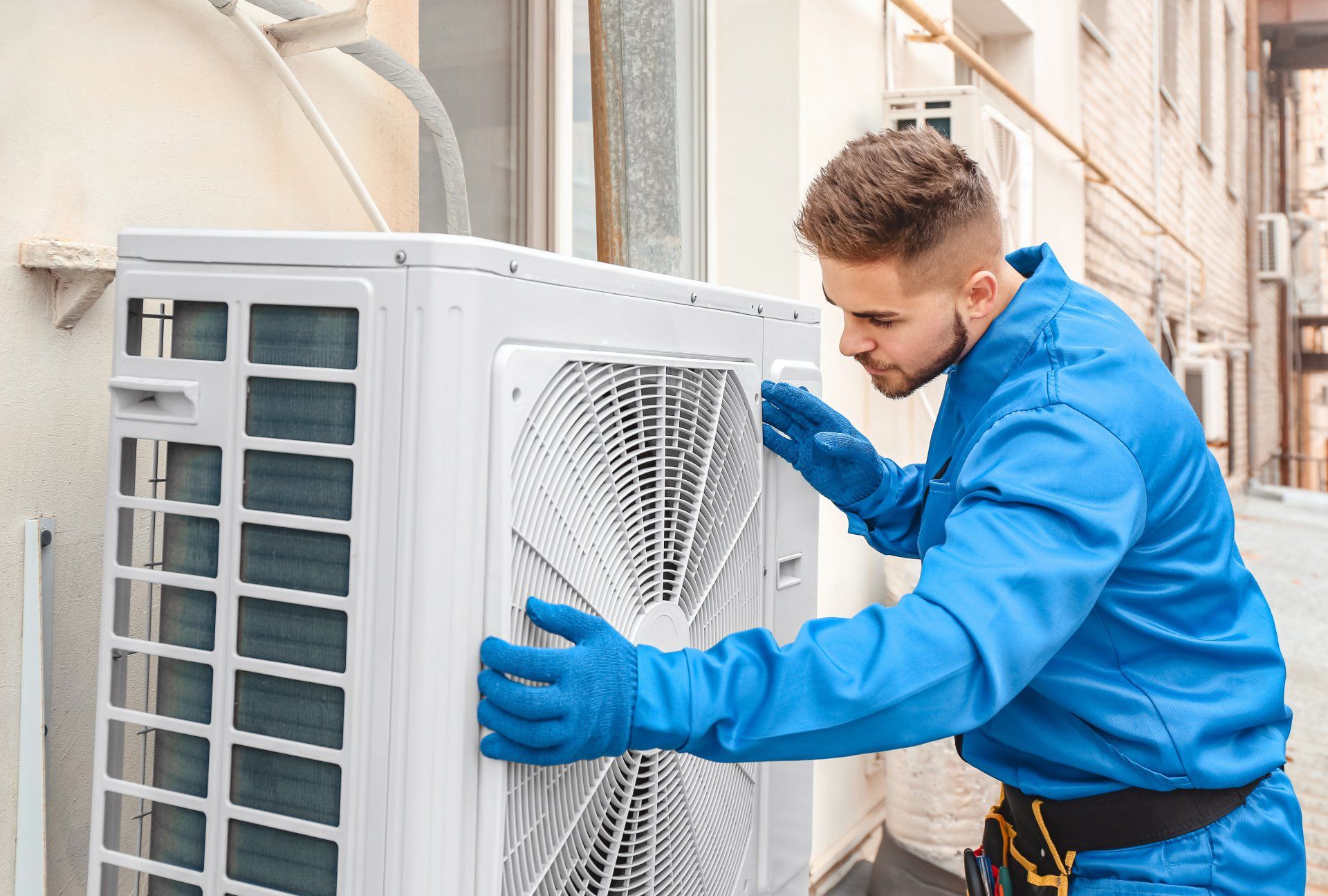 HVAC technician in blue overalls fixing an outdoor air conditioning unit.