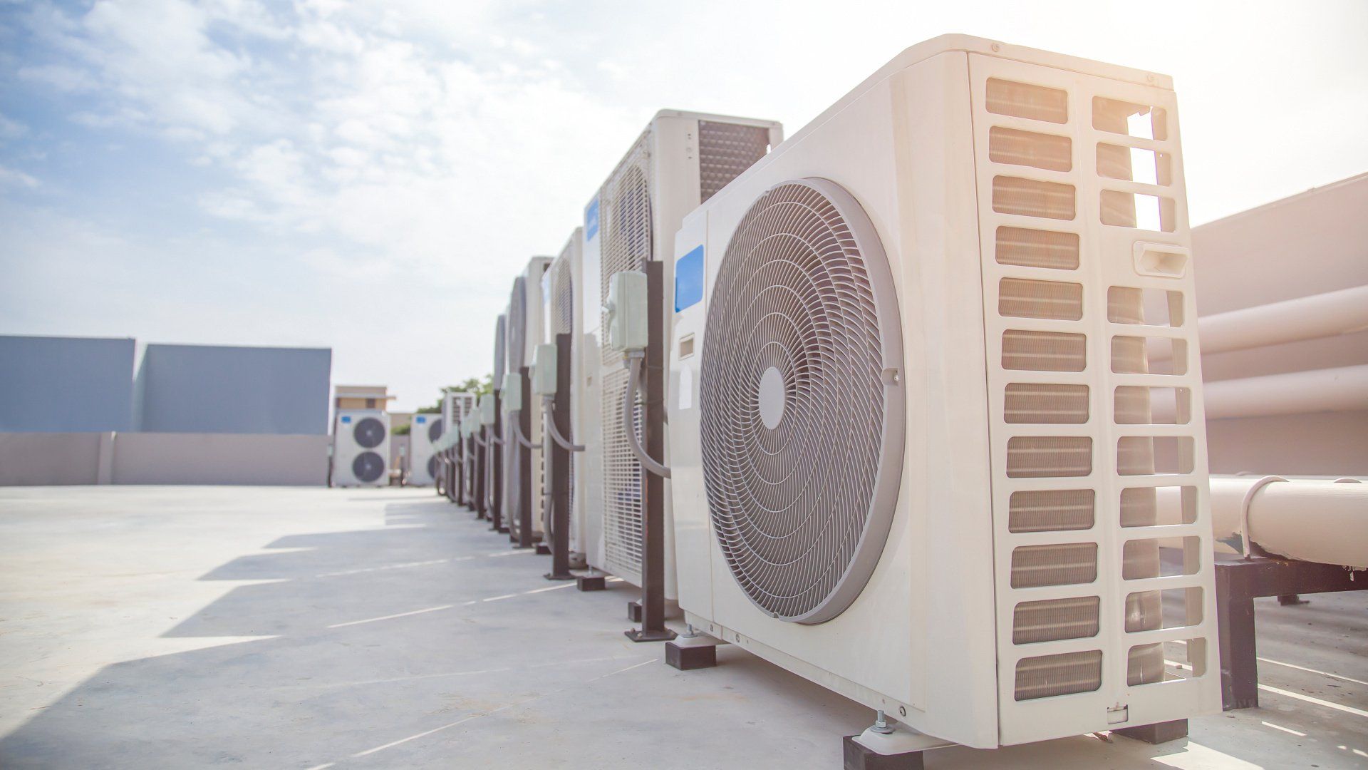 Row of air conditioning units on a rooftop under a sunny sky.