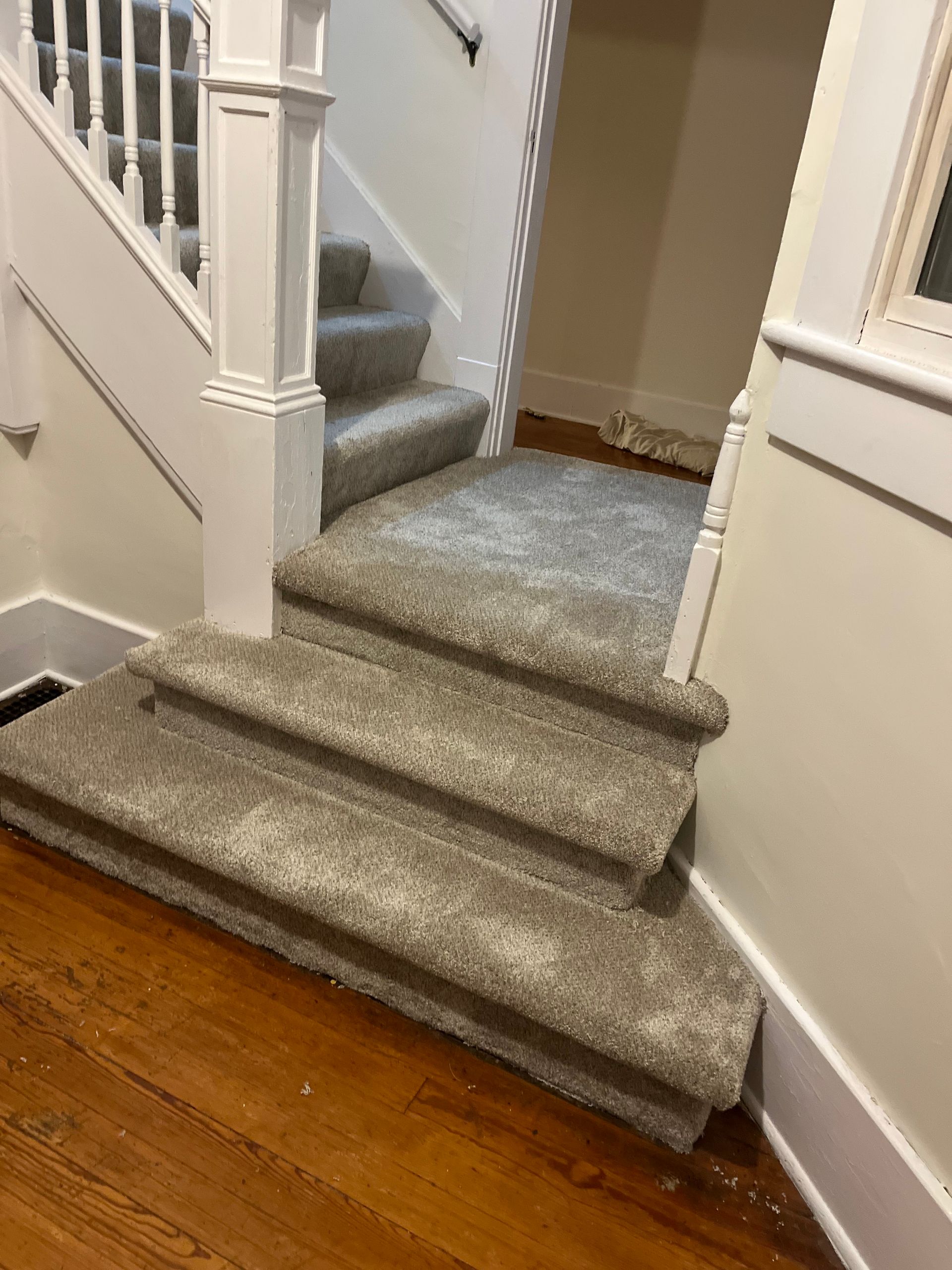 Carpeted staircase with white banisters and a hardwood floor at the bottom.