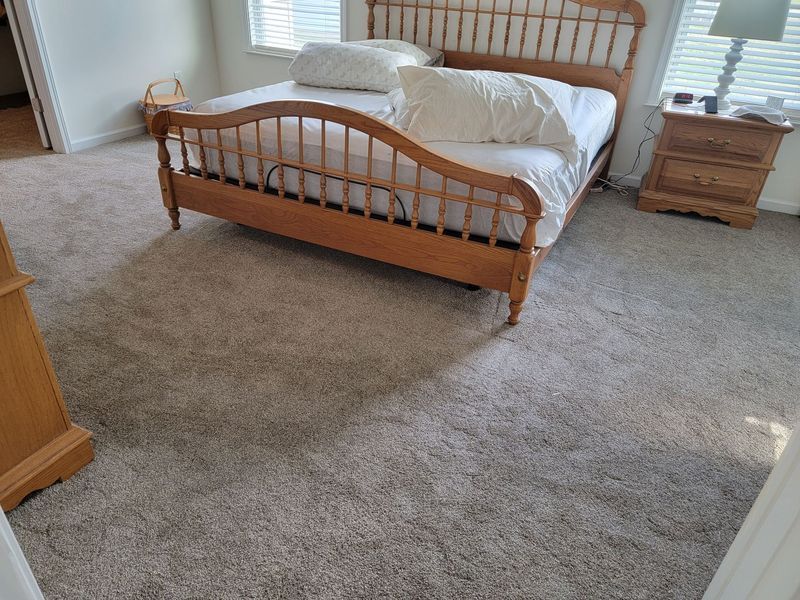 Bedroom with wooden bed, beige carpet, nightstand, and window with blinds