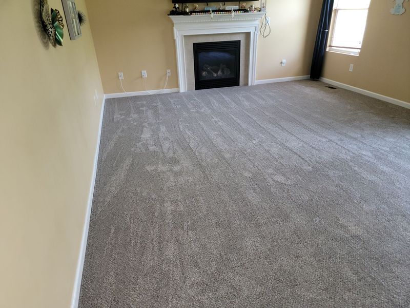 Empty beige living room with gray carpet and a fireplace at the far end