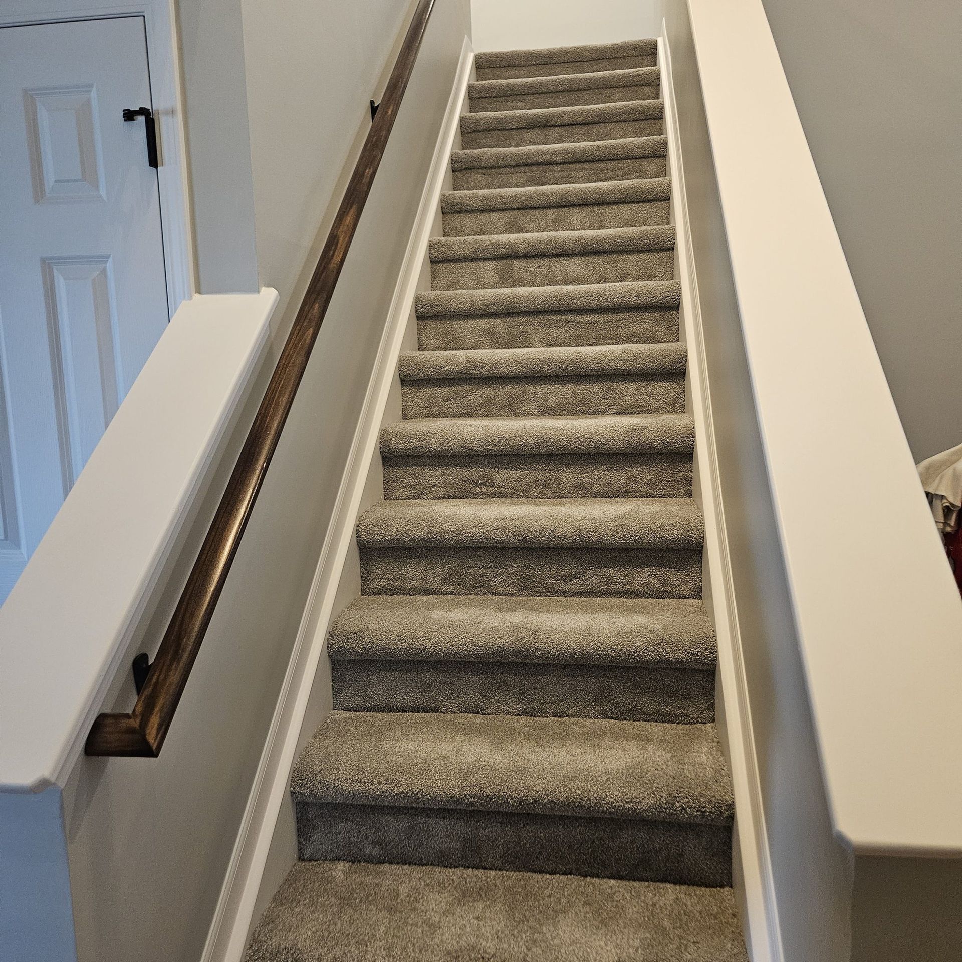 Carpeted staircase with wooden handrail in a light-colored home interior.
