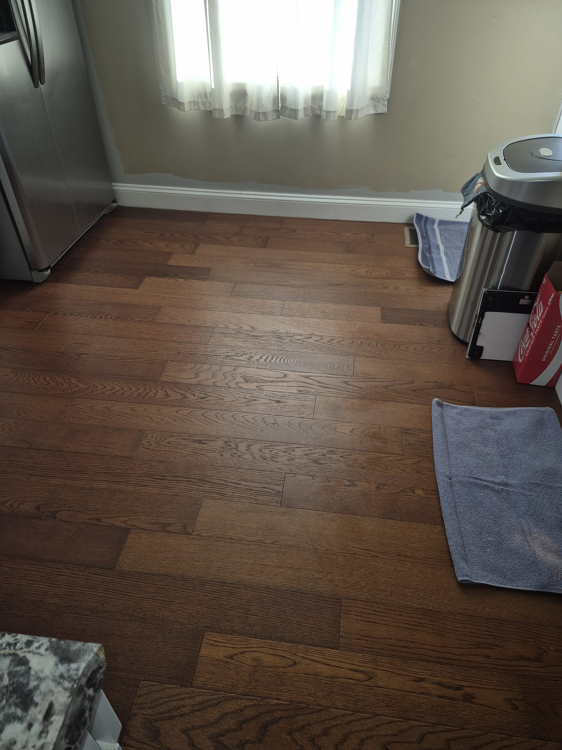 Wooden floor with two rugs, a window, and a trash can in a small room