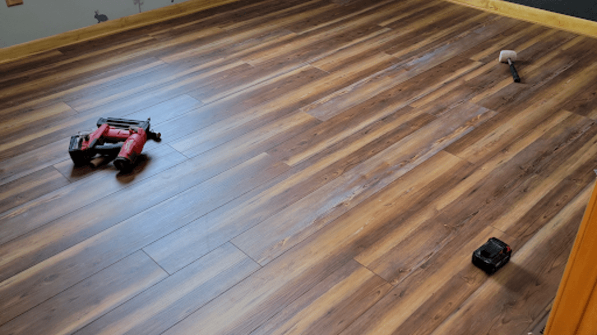 Three small toy vehicles on a wood floor, including a red remote-control car and a black car.