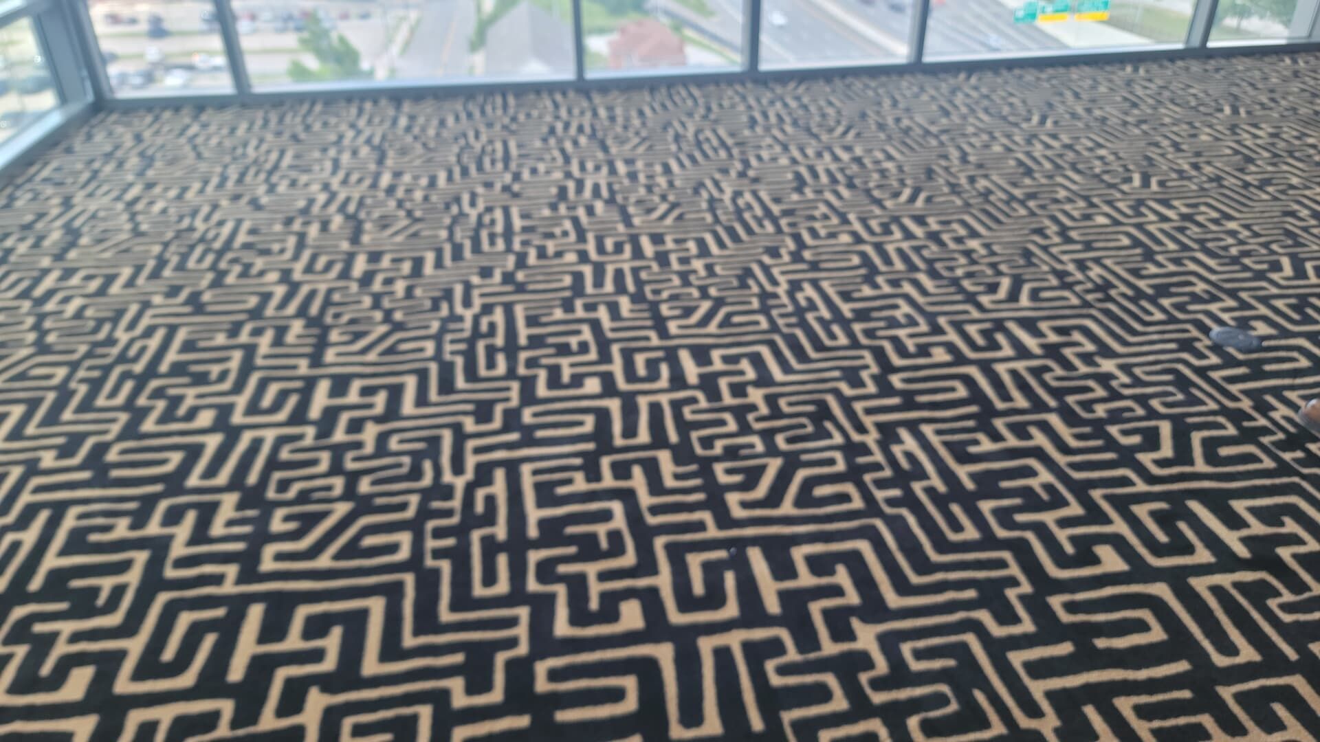 Black-and-gold geometric maze-pattern carpet in a bright indoor room with windows.