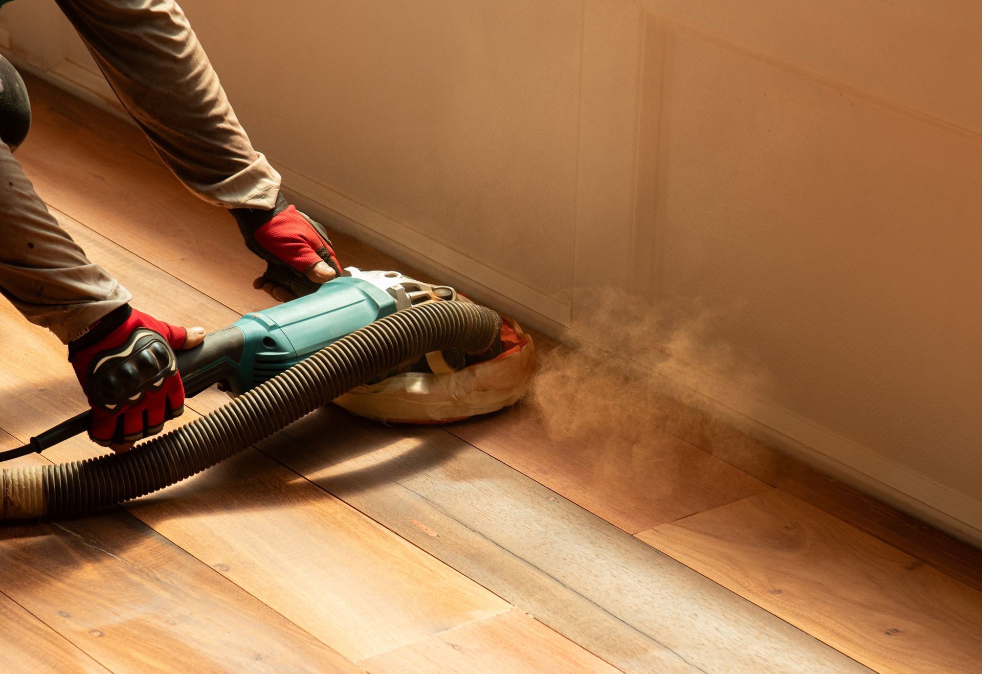 Vacuuming dust from a hardwood floor along a wall, with gloved hands holding the vacuum nozzle