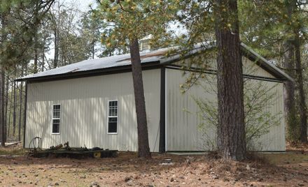 Small beige metal shed with a dark roof in a wooded area