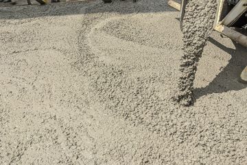 Concrete being poured onto a construction site surface, with a worker’s boot visible at right