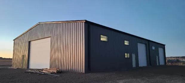 Metal storage building with ribbed gray siding and large roll-up doors on a gravel lot at sunset