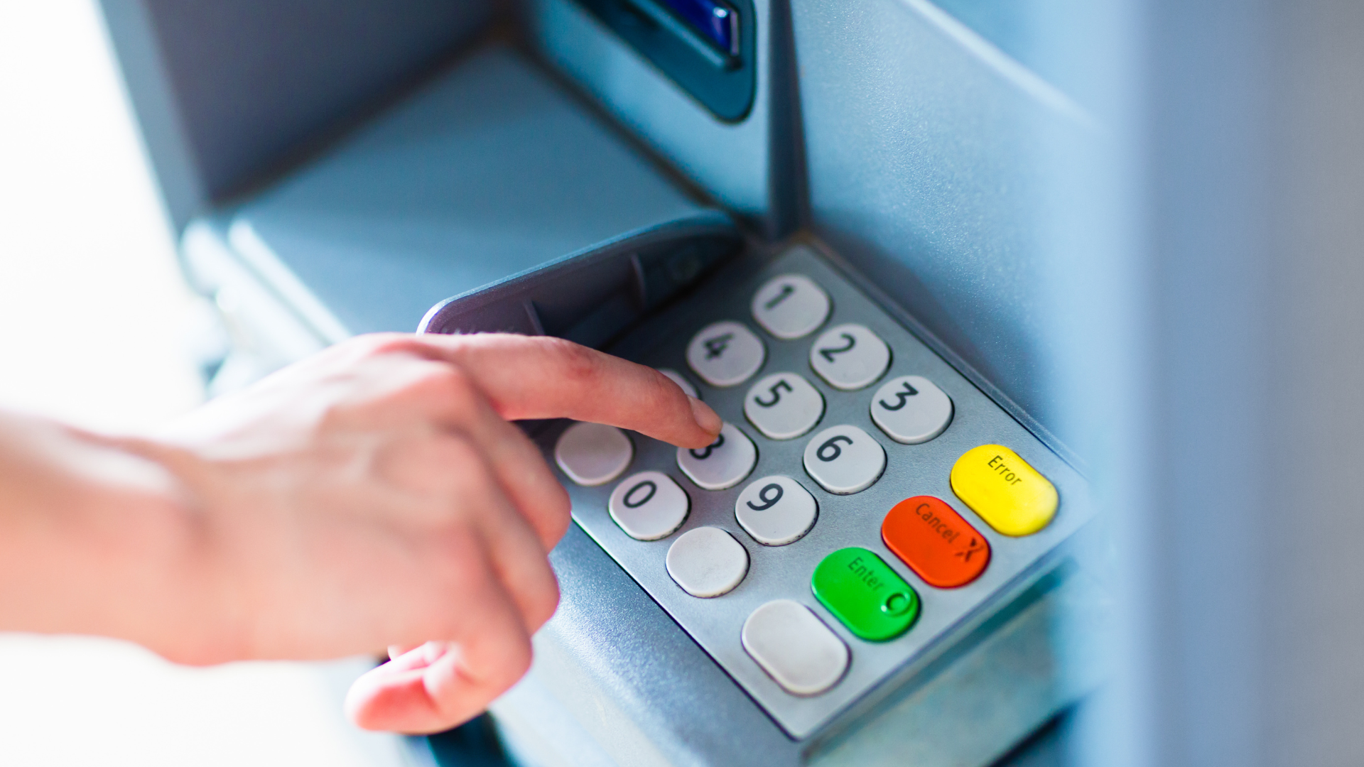 Hand entering a PIN on an ATM keypad, likely withdrawing money.