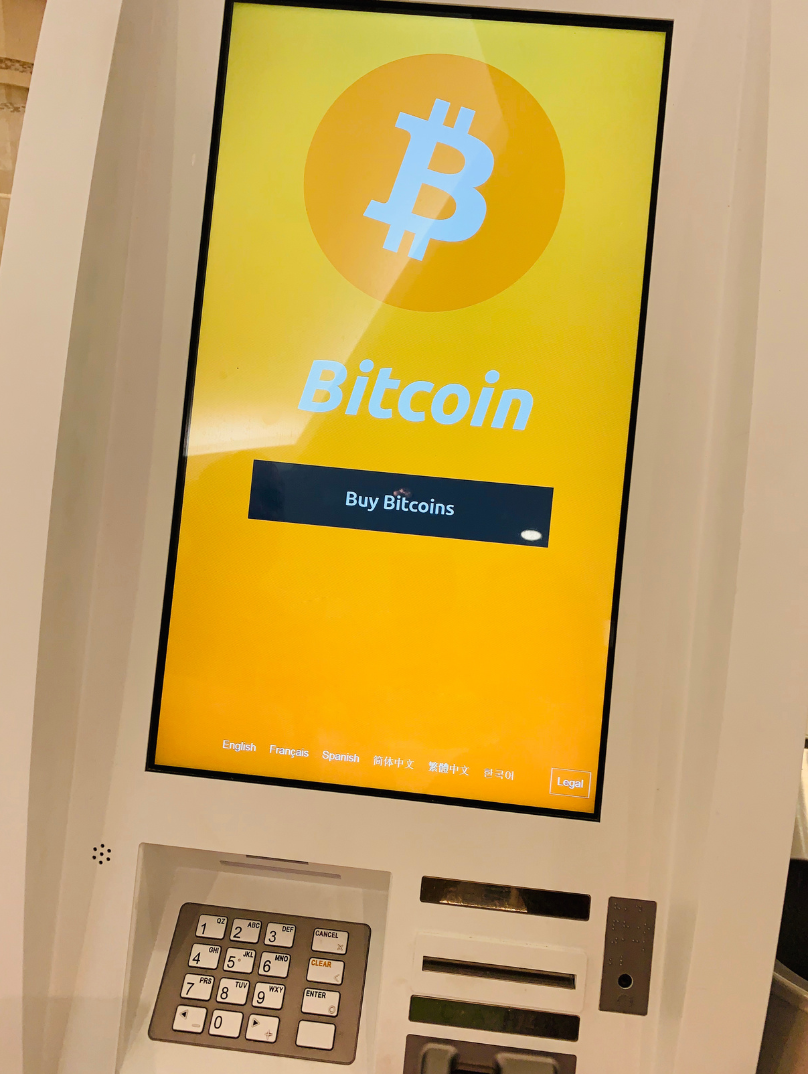 Bitcoin ATM with a bright yellow screen displaying the Bitcoin logo and word
