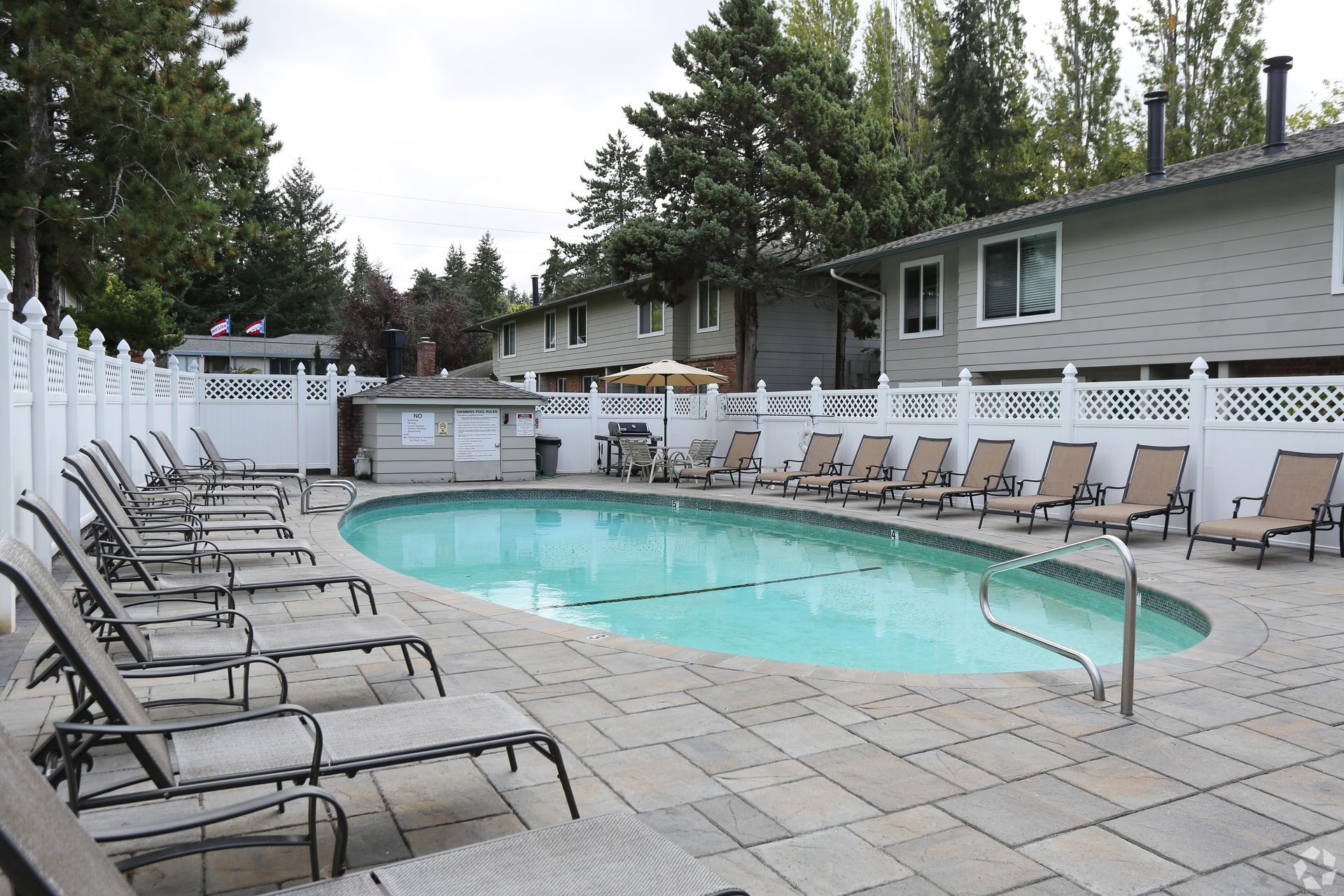 Pool surrounded by lounge chairs, in front of a residential building.
