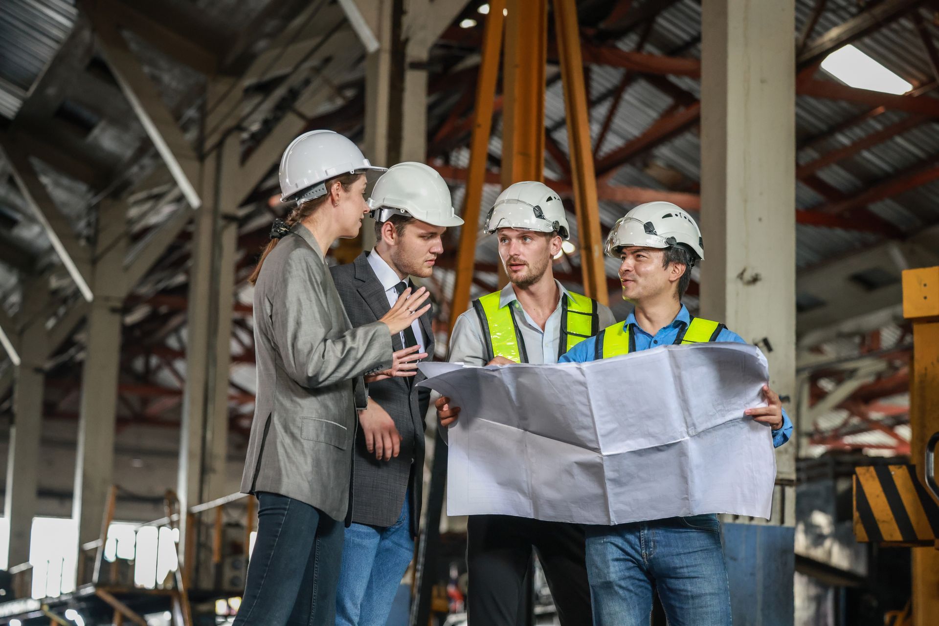 A group of construction workers are standing in a warehouse looking at a blueprint.