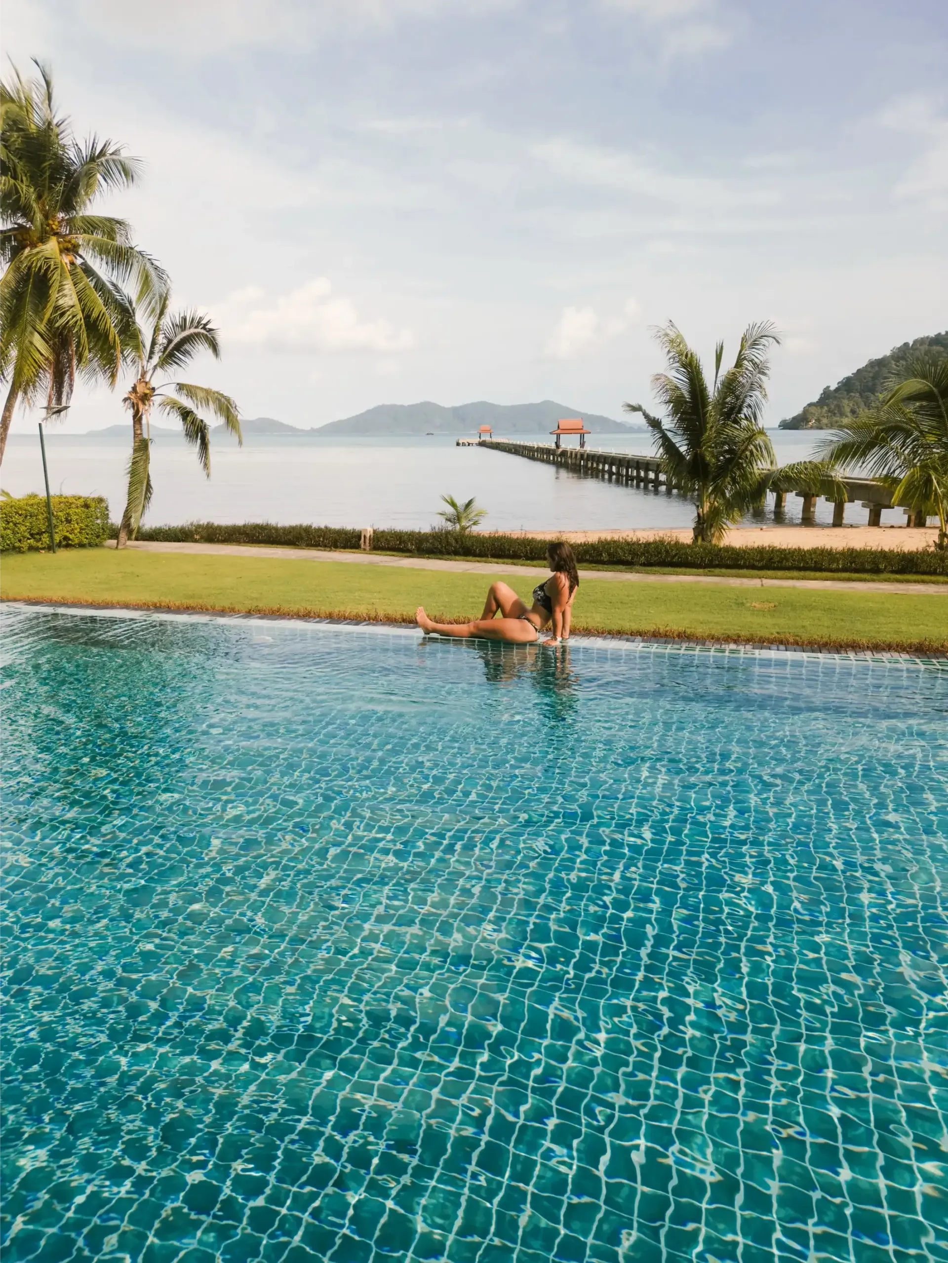Two people are swimming in a swimming pool near the ocean.