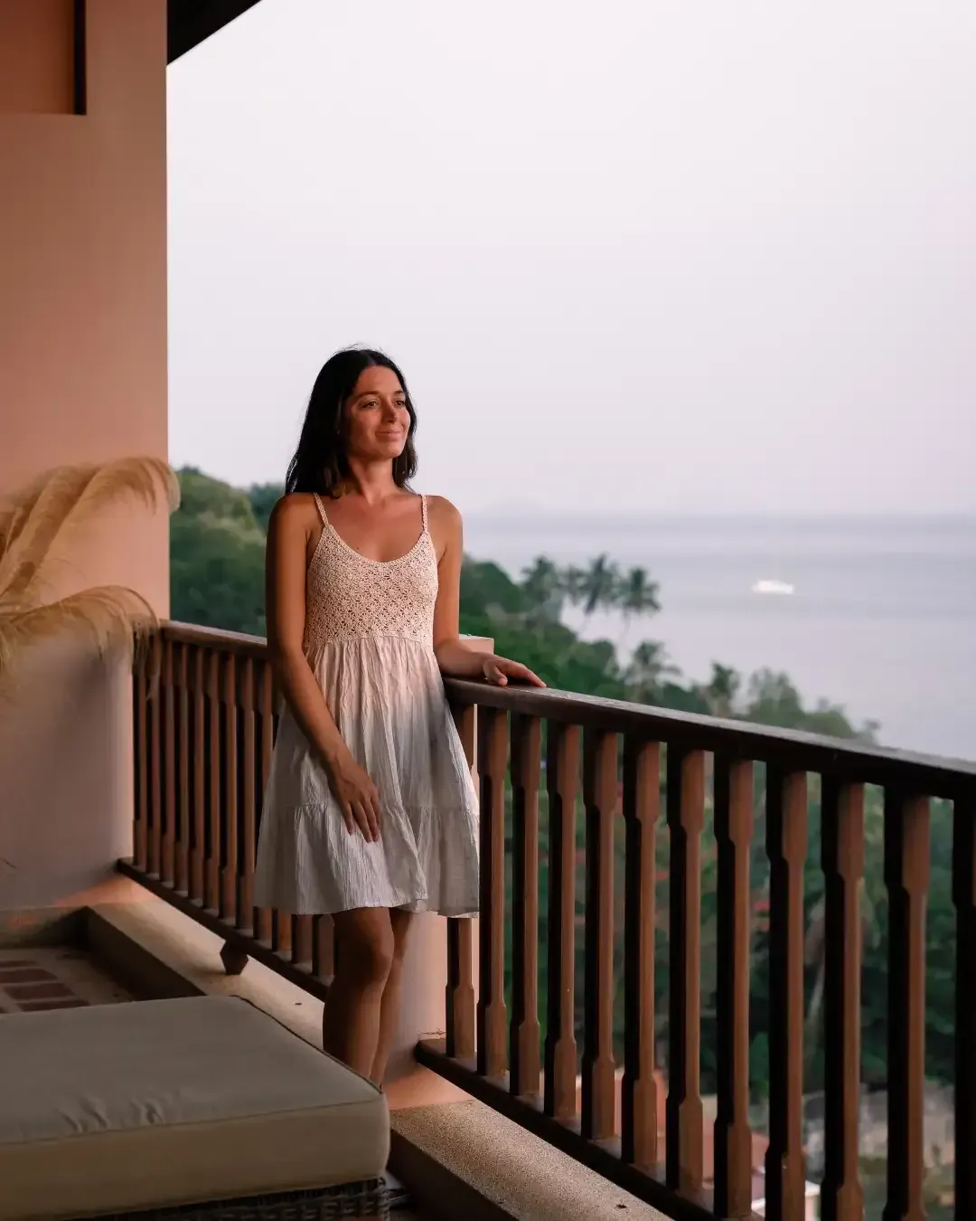 A woman in a white dress is standing on a balcony overlooking the ocean.