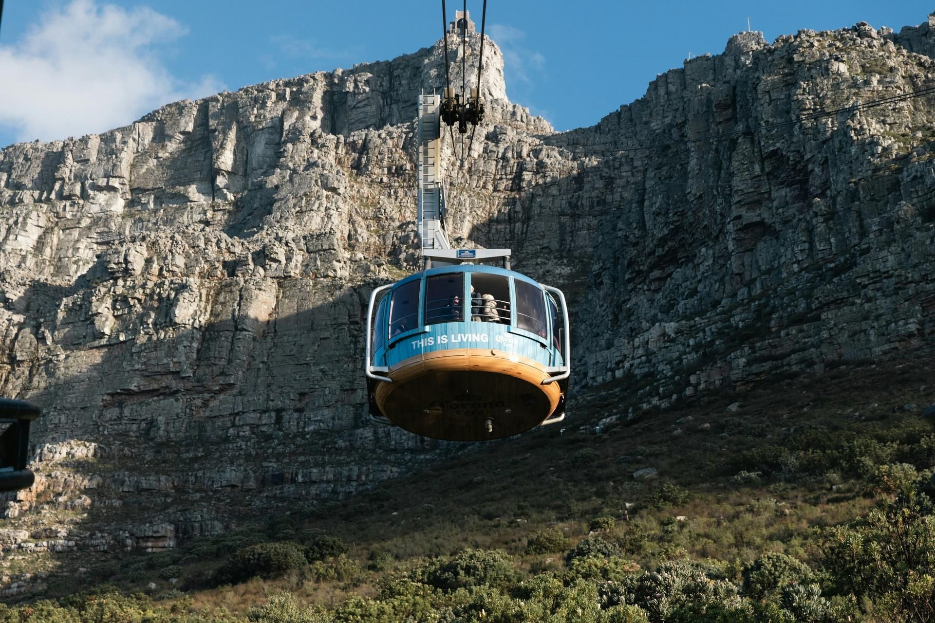 Blue cable car traveling past a rocky cliff under a clear sky.