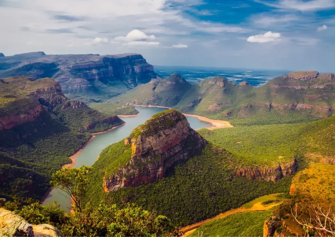 Aerial view of a lush canyon with a winding river and steep rocky cliffs under a blue sky