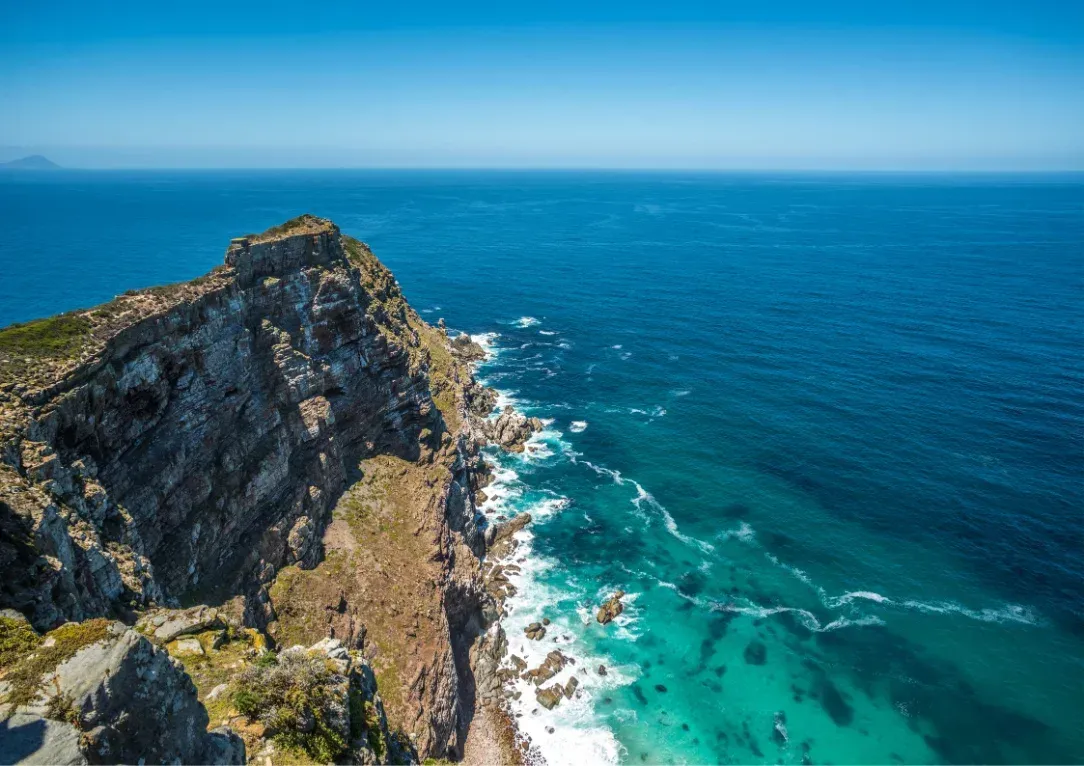 Rocky coastal cliff with turquoise waves and deep blue ocean under clear sky