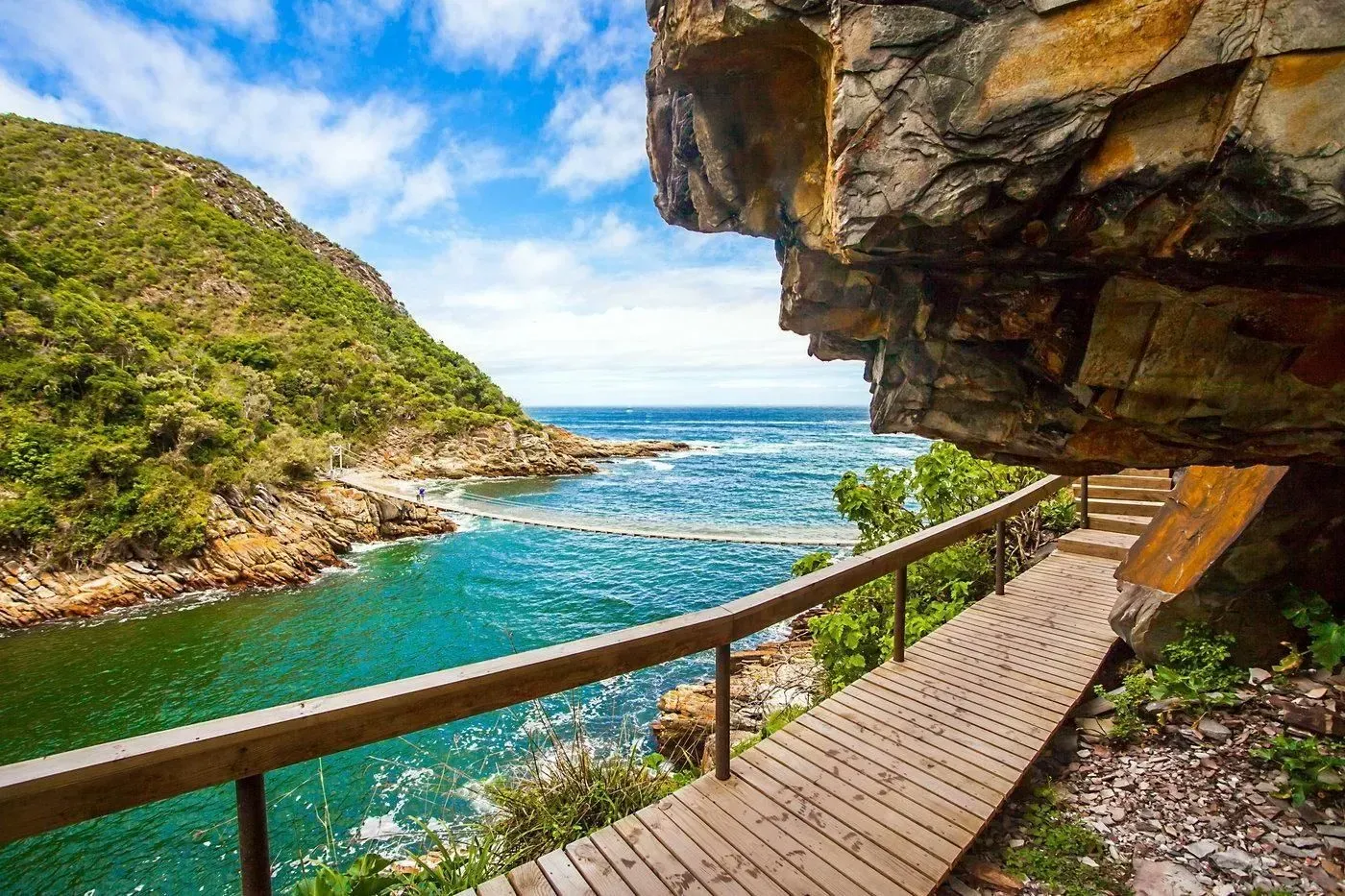 Cliffside boardwalk beside turquoise sea and rocky cove under a shaded overhang